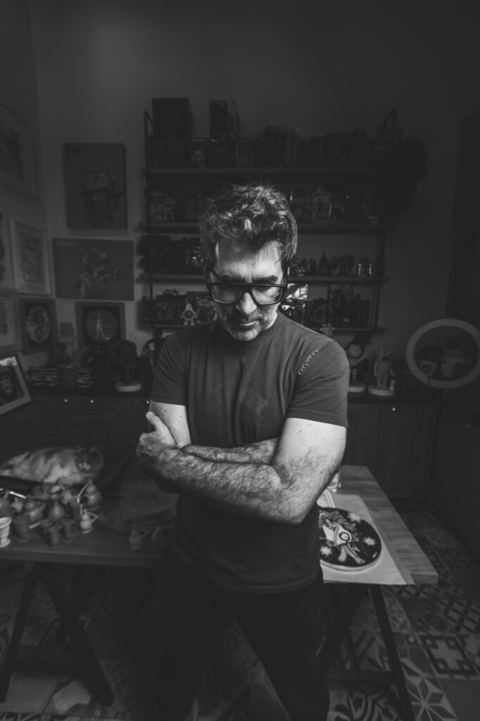 Rafa Lanfranco de brazos cruzados en su taller, rodeado de esculturas, cerámicas y obra enmarcada.